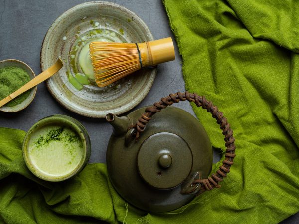 Hot green tea in a glass with cream topped with green tea, decorated with green tea powder.